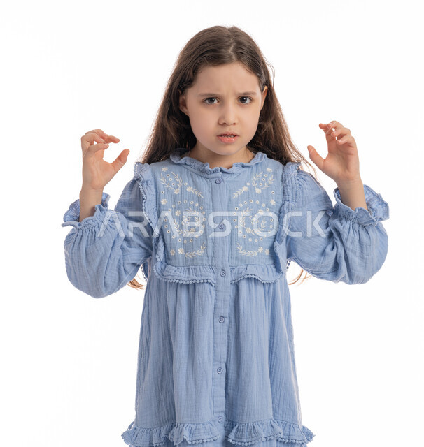 Anger over something, a Saudi girl standing with hand and face gestures indicating boredom, dissatisfaction and dissatisfaction, a close-up portrait of an Arab Emirati Gulf girl wearing a dress, raising her hands up with nervous expressions, white background.