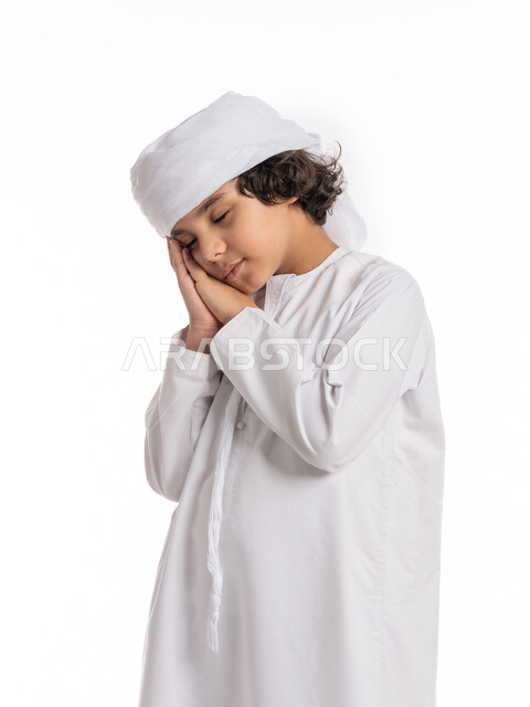 الشعور بالتعب و الحاجه الى النوم والراحه, الإحساس بالكسل و الإرهاق والخمول، بورتريه مقرب لولد عربي اماراتي خليجي يرتدي الكندورة والعمامة يضع يديه تحت رأسه, فتى سعودي يقف بإيماءات وجه ويدين تدل على النعاس, خلفية بيضاء