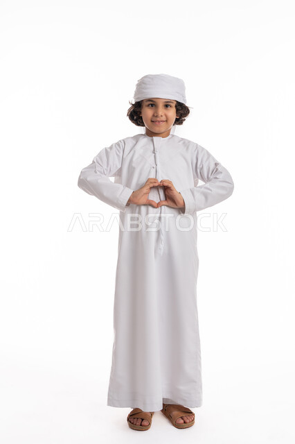 إيماءات وتعابير الشعور بالحب, فتى سعودي يقوم بالاحتفال بعيد الحب (الفالنتاين)، التعبير عن المشاعر الإيجابية، السعاده والطمأنينه والمحبه, بورتريه لولد عربي اماراتي خليجي يرتدي الكندورة والعمامة يرفع يديه بشكل قلب, صورة الجسم بالطول الكامل، خلفية بيضاء
