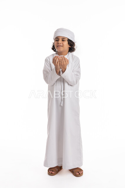 الحمد والشكر و طلب العون, فتى سعودي يطلب المغفره من الله تعالى، الرغبه في تحقيق الأمنيات, بورتريه لولد عربي اماراتي خليجي يرتدي الكندورة والعمامة بإيماءات وجه ويدين تدل على الدعاء والتضرع الى الله, صورة الجسم بالكامل، خلفيه بيضاء