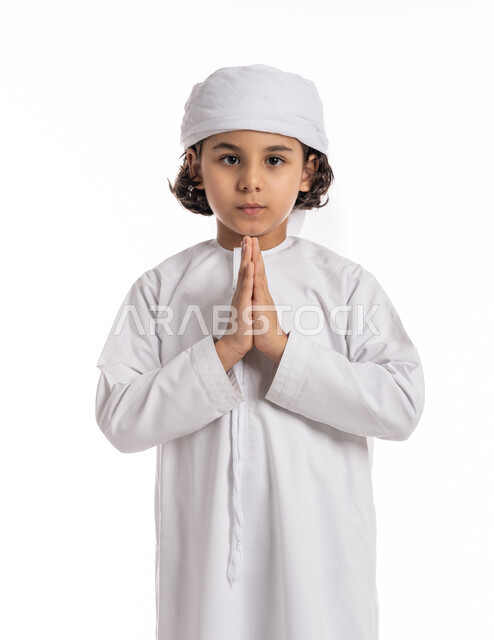 النظر الى الكاميرا بتعابير وحركة يد تدل على الشكر والتقدير والاحترام، بورتريه مقرب لولد عربي خليجي إماراتي يرتدي العمامة والكندورة يقف باستقامة بتعابير الحمد والامتنان، فتى سعودي مبتسم يقوم بالاستئذان وطلب شيء ما، خلفية بيضاء