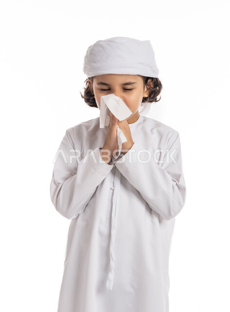فتى سعودي يستخدم المناديل الورقيه للعطس, التهابات الأنف التحسسية, الحاجة الى العلاج والدواء, بورتريه مقرب لولد عربي اماراتي خليجي يرتدي العمامة والكندورة بإيماءات وجه ويدين تدل على العطاس, الشعور بالمرض و الزكام, خلفية بيضاء
