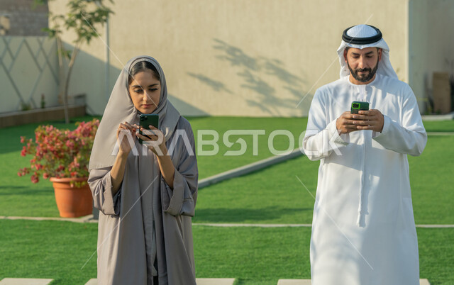Using modern technical and technological devices, communicating and chatting with friends and relatives via mobile phone, an Arab Gulf Emirati couple holding a mobile phone, spending enjoyable times in one of the tourist chalets, hiking in the open air, following news on social media sites.