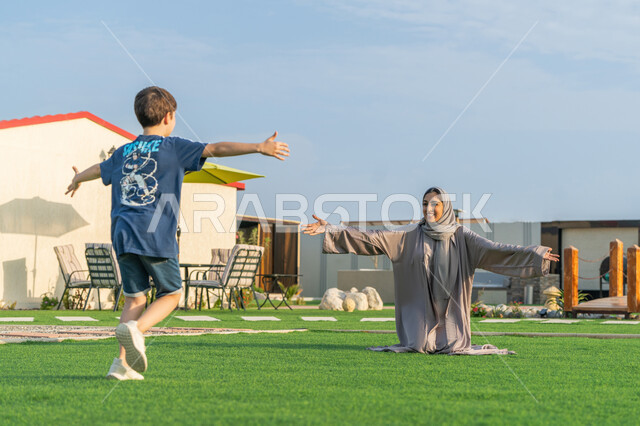 رحلة ترفيهية سياحية, اللعب و التسلية مع الابناء, عطلة صيفية وأجواء عائلية سعيدة، التنزه في الهواء الطلق، عائلة عربية خليجية اماراتية تقضي أوقات ممتعة في إحدى الشاليهات السياحية بالامارات, امراة عربية خليجية اماراتية ترتدي العباءة الملونة تقوم بعناق ابنها