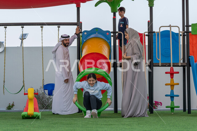 مشاركة الاطفال بالانشطة الترفيهية، التنزه مع الوالدين, مفهوم الأسره السعيده, التزحلق على الزحليقه, استغلال وقت الفراغ في التسلية واللعب, طفلان عربيان خليجيان اماراتيان يستمتعان باللعب بالمنتزه, الإستمتاع باللعب في يوم مشمس, قضاء أوقات ممتعة في الحديقة