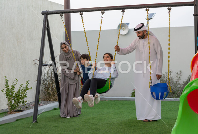 الإستمتاع باللعب في يوم مشمس, التأرجح على الأرجوحه, عائلة عربية خليجية اماراتية تقضي أوقات ممتعة في حديقة ترفيهية، قضاء الوقت مع الابناء, رجل عربي خليجي اماراتي يرتدي الكندورة والغترة البيضاء، استغلال وقت الفراغ في التسلية والمرح
