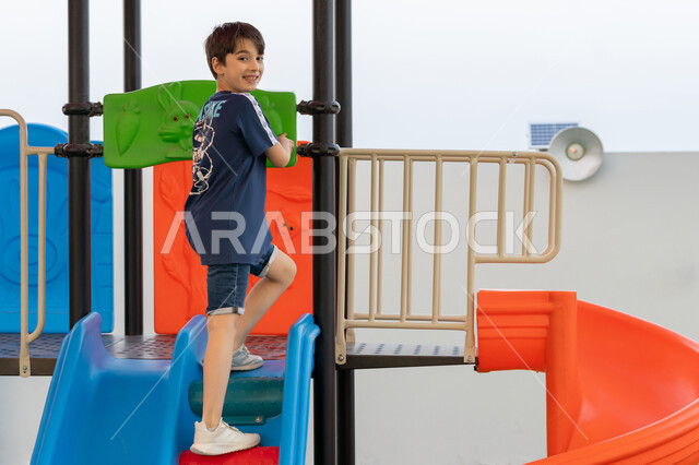 استغلال وقت الفراغ في التسلية واللعب, ايماءات المرح و السرور, طفل عربي اماراتي خليجي يلعب في المنتزه, التزحلق على الزحليقه, الإستمتاع باللعب في يوم مشمس, يقضي أوقات ممتعة في حديقة ترفيهية