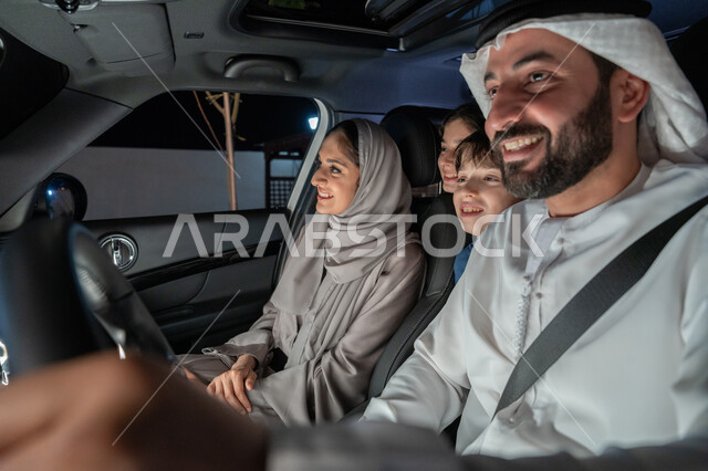 الإلتزام بربط حزام الأمان، رحله جماعيه في السياره, عائلة عربيه خليجية اماراتية سعيدة في رحلة بالسيارة يقومون بالتنزه في شوارع الامارات العربية المتحدة،  دردشه ومحادثات في الطريق، قضاء وقت ممتع مع العائله، رجل عربي خليجي اماراتي يرتدي الكندورة والغترة البيضاء