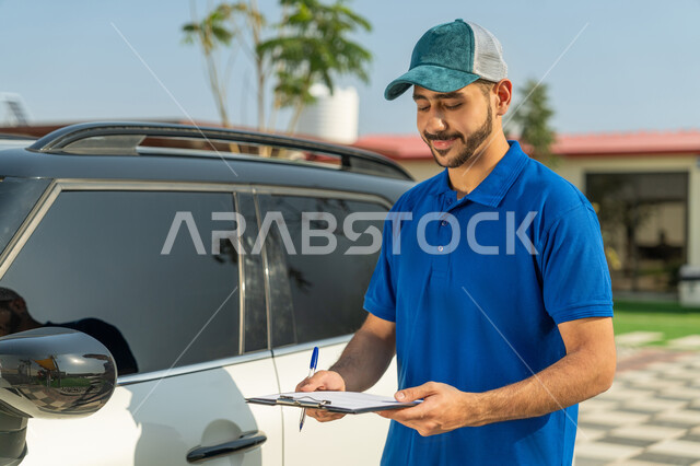 Customer services and delivery of goods and orders to customers, a smiling Emirati Gulf Arab worker wearing a casual outfit and a blue hat standing next to the mail car and carrying papers and documents for receiving and delivering packages with expressions of satisfaction and confidence, express delivery services in the Emirates