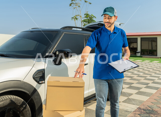 خدمة العملاء وعملية التوصيل السريعة في الإمارات, تسليم البضائع والطلبات للزبائن، عامل إماراتي خليجي عربي إماراتي مبتسم يرتدي الزي الكاجوال يجمل بيده أوراق ومستندات استلام وتسليم الطرود، التأكد من صحة الطلبية بتعابير السرور والرضا