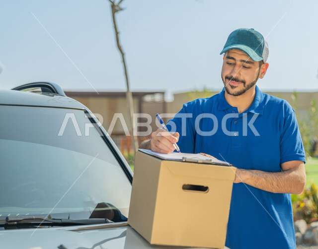 خدمة العملاء وتوصيل الطلبات، صورة مقربة لعامل إماراتي خليجي عربي يرتدي الزي الكاجوال يقف بجانب السيارة، التوقيع على أوراق ومستندات استلام وتسليم الطرود، تسليم البضائع والطلبات للزبائن، أمارات الرضا والسرور