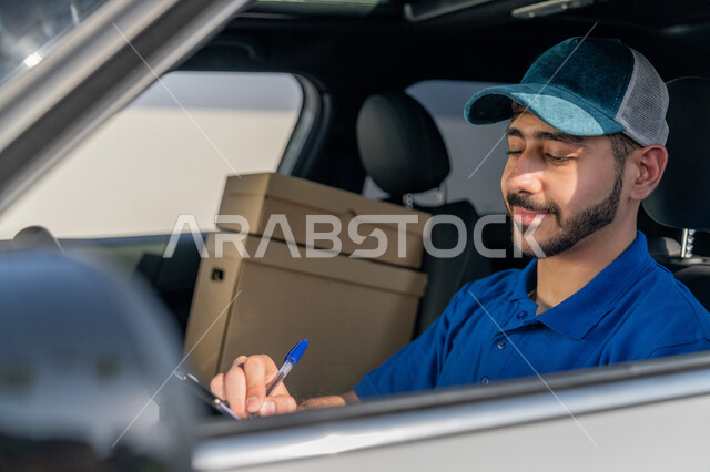 صورة مقربة لمندوب عربي خليجي إماراتي مبتسم يرتدي الزي الكاجوال و القبعة الزرقاء يجلس داخل السيارة وتبدو عليه تعابير البشاشة والرضا، التوقيع على أوراق ومستندات استلام وتسليم الطرد, خدمات الشحن والتوصيل السريعة في الامارات