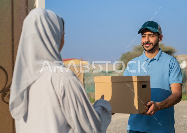 عمليات الشحن و التوصيل ذات الجودة العالية, مندوب عربي إماراتي خليجي يرتدي الزي  الكاجوال يقف مع العميل عند الباب بتعابير السرور ,تسليم واستلام البضائع و المشتريات, خدمة الديلفري الآمنة,توصيل طلبيات الاونلاين السريع