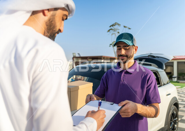 خدمة العملاء وعملية التوصيل السريعة في الامارات, توصيل طلبيات الاونلاين السريع, مندوب توصيل يرتدي لبس كاجوال يقف مع العميل بجانب سيارة شحن البضائع بتعابير السرور, التوقيع على أوراق تسليم واستلام المشتريات