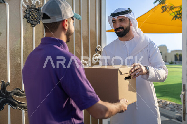 خدمة الديلفري الآمنة ,توصيل طلبيات الاونلاين السريع, عميل عربي يقف مع مندوب التوصيل عند الباب بتعابير الرضا, تسليم واستلام البضائع والمشتريات, عمليات الشحن ذات الجودة العالية