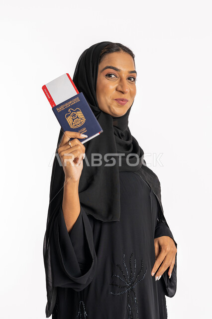 Taking recreational tours during vacation time, a close-up portrait of a veiled Arab Gulf Emirati woman wearing a black abaya, holding a passport and a ticket in her hand, looking at the camera with happy gestures, an elegant young Saudi woman, preparing for an enjoyable summer trip, tourism and travel concept, white background