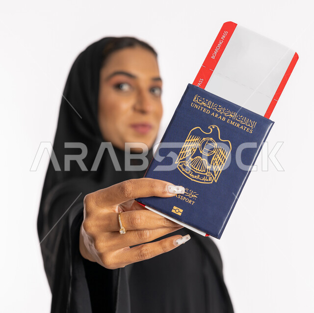 إيماءات السرور والفرح، تعابير البهجة والسعادة، مفهوم السياحة والسفر، القيام بالجولات الترفيهية في وقت الإجازة، بورتريه مقرب لإمرأة عربية خليجية اماراتية محجبة ترتدي عباءة سوداء ترفع الباسبور والتيكت، شابة سعودية أنيقة، خلفية بيضاء