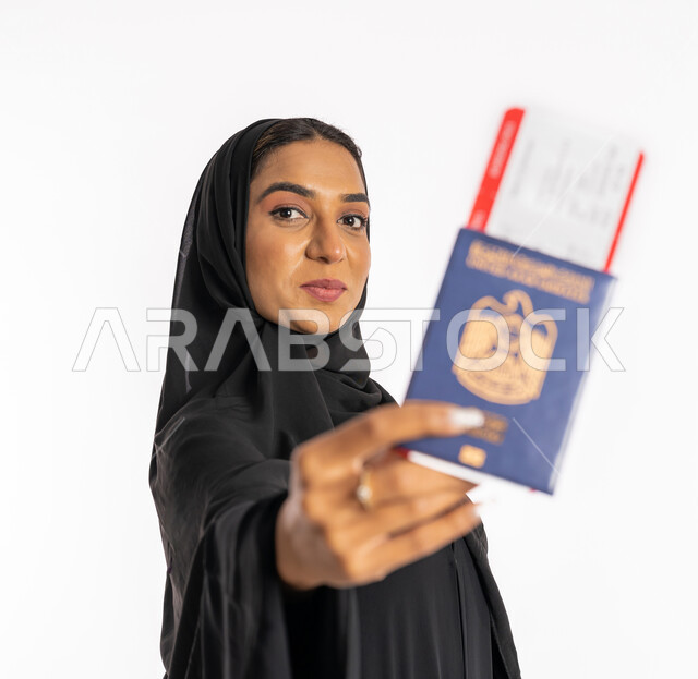 تعابير البهجة والسرور، إيماءات السرور والفرح، مفهوم السياحة والسفر، القيام بالجولات الترفيهية في وقت الإجازة، بورتريه مقرب لإمرأة عربية خليجية اماراتية محجبة ترتدي عباءة سوداء ترفع الباسبور والتيكت، شابة سعودية أنيقة، خلفية بيضاء