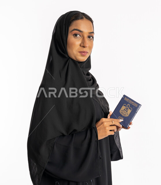 شابة سعودية أنيقة، تعابير البهجة والسرور، إيماءات السرور والفرح، مفهوم السياحة والسفر، القيام بالجولات الترفيهية في وقت الإجازة، بورتريه مقرب من الجانب لإمرأة عربية خليجية اماراتية محجبة ترتدي عباءة سوداء تحمل بيدها الباسبور، خلفية بيضاء