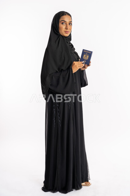 القيام بالجولات الترفيهية في وقت الإجازة، بورتريه من الجانب لإمرأة عربية خليجية اماراتية محجبة ترتدي عباءة سوداء تحمل بيدها الباسبور، شابة سعودية أنيقة، تعابير البهجة والسرور، إيماءات السرور والفرح، مفهوم السياحة والسفر، صورة لكامل الجسم، خلفية بيضاء