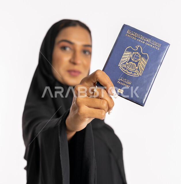تعابير البهجة والسرور، ايماءات السرور والفرح، مفهوم السياحة والسفر، القيام بالجولات الترفيهية في وقت الإجازة، بورتريه مقرب لإمرأة عربية خليجية اماراتية محجبة ترتدي عباءة سوداء ترفع الباسبور، شابة سعودية أنيقة، خلفية بيضاء
