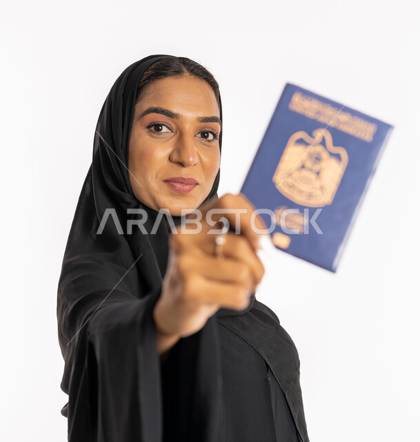 تعابير البهجة والسرور، ايماءات السرور والفرح، مفهوم السياحة والسفر، القيام بالجولات الترفيهية في وقت الإجازة، بورتريه مقرب لإمرأة عربية خليجية اماراتية محجبة ترتدي عباءة سوداء ترفع الباسبور، شابة سعودية أنيقة، خلفية بيضاء
