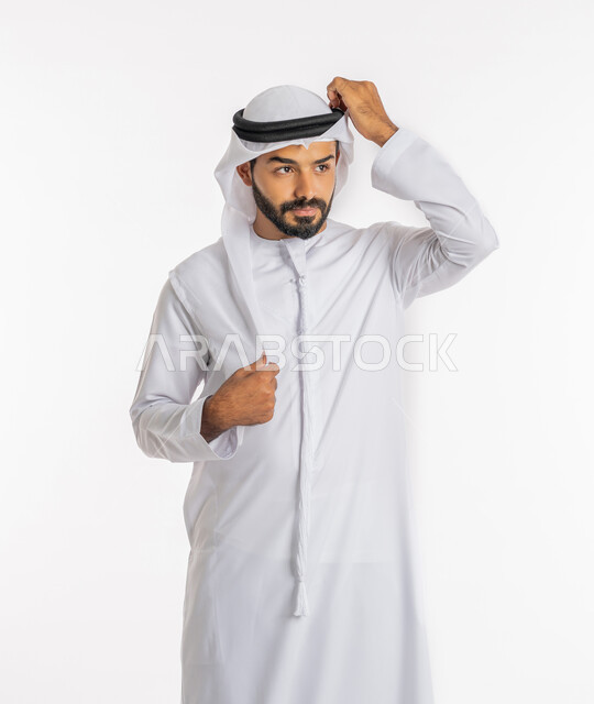 Preparing to leave the house, the concept of elegance and masculinity, looking at a place with gestures of contemplation and concentration, expressions of joy and happiness, concern for external appearance, a portrait of an Emirati Gulf Arab man wearing the traditional Emirati dress adjusting the ghutra, white background