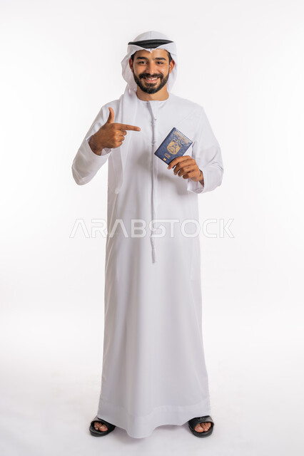 تعابير البهجة والسرور، إيماءات السرور والفرح، مفهوم السياحة والسفر، شعار دولة الامارات العربية المتحدة، تأشيرة سفر دولية، بورتريه لرجل عربي خليجي اماراتي يرتدي الكندورة والغترة يشير باصبع السبابة للباسبور، صورة لكامل الجسم، خلفية بيضاء