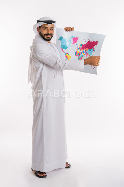 مفهوم السياحة والسفر، البحث والاستكشاف حول العالم، تحديد مسار سير الرحلة، القيام بجولات سياحية ترفيهية، بورتريه من الجانب لرجل عربي خليجي اماراتي يرتدي الكندورة والغترة يحمل بيده الخريطة، صورة لكامل الجسم، خلفية بيضاء