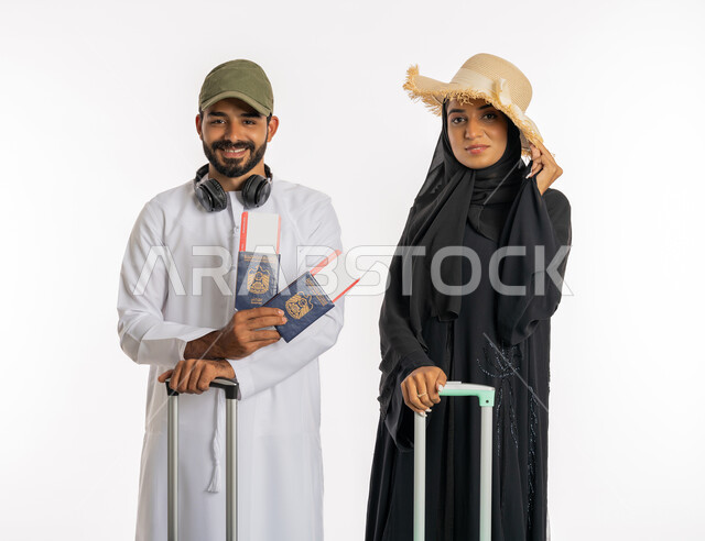 ايماءات السرور والسعادة، الاستعداد لقضاء رحلة صيفية ممتعة، انتظار موعد الطائرة، بورتريه زوجان عربيان اماراتيان يرتديان القبعات يحملان جواز وتأشيرة السفر يمسكان بحقائب الامتعة، مفهوم السياحة والقيام بالجولات الترفيهية في وقت الإجازة، خلفية بيضاء