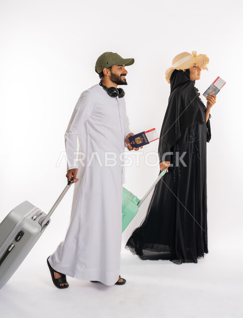 إيماءات السعادة والحماس، بورتريه من الجانب لزوجان عربيان اماراتيان يرتديان القبعات يحملان جواز وتأشيرة السفر يمسكان بحقائب الامتعة، الاستعداد لقضاء رحلة صيفية ممتعة، مفهوم السياحة والقيام بالجولات الترفيهية في وقت الإجازة، صورة لكامل الجسم، خلفية بيضاء