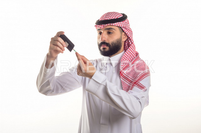 بورتريه لشاب سعودي خليجي يعاني من داء السكري ، مشاكل ارتفاع السكر في الدم ، جهاز قياس السكر في الدم خاص لمرضى السكري  ، حالة مرضية ،  خلفية بيضاء