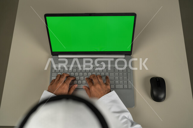 متابعة آخر أخبار السوشال ميديا، استخدام الأجهزة الحديثة في انجاز المهام, عرض شاشة خضراء كروما عبر الحاسوب المحمول، صورة من الاعلى لرجل عربي خليجي اماراتي يرتدي الكندورة والغترة البيضاء, الدردشة والمحادثات مع الأصدقاء، استعمال التكنولوجيا في العمل عن بعد