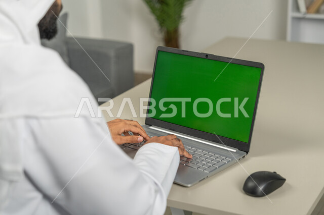 تصفح مواقع التواصل الاجتماعي، استخدام الأجهزة الحديثة في انجاز المهام, عرض شاشة خضراء كروما عبر الحاسوب المحمول، صورة من الخلف لرجل عربي خليجي اماراتي يرتدي الكندورة والغترة البيضاء, الدردشة والمحادثات مع الأصدقاء، استعمال التكنولوجيا في العمل عن بعد
