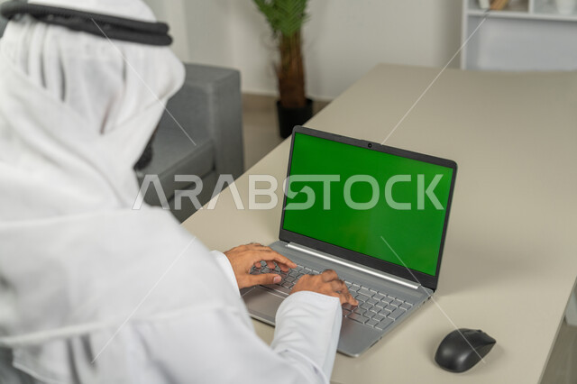 استخدام الأجهزة الحديثة في انجاز مهام الأعمال، برامج التواصل الاجتماعي, عرض شاشة خضراء كروما عبر الحاسوب المحمول، صورة من الخلف لرجل عربي خليجي اماراتي يرتدي الكندورة والغترة البيضاء, الدردشة والمحادثات مع الأصدقاء، استعمال التكنولوجيا في العمل عن بعد