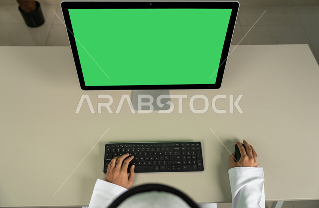 مشاهدة الأفلام والمسلسلات، استخدام الكمبيوتر المكتبي بخلفية خضراء كروما، الدردشة والمحادثات والتواصل الاجتماعي , التسويق لموقع إلكتروني، صورة من الاعلى لرجل عربي خليجي اماراتي يرتدي الكندورة و الغترة البيضاء ، إجراء مكالمة فيديو