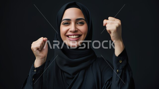 Gestures of joy at the completion of a certain thing, looking at the camera with expressions of victory and gain, the concept of success and achieving goals, a portrait of a veiled Saudi Arabian Gulf woman wearing a black abaya, raising her hands upward with movements of encouragement and enthusiasm, a black background.