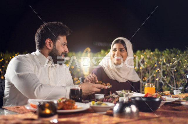 زوجان سعوديان خليجيان على مائدة الافطار بشهررمضان ، مشاركة الاجواء الرمضانية الرائعة بالهواء الطلق ، سفرة مليئة بأصناف من المأكولات العربية السعودية اللذيذة ، شهر رمضان ، رمضان كريم ، فانوس رمضان