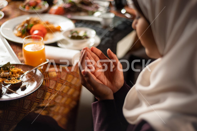 A Saudi Arabian couple at the breakfast table in the month of Ramadan, raising hands and praying to God with praise and thanksgiving, a trip full of varieties of delicious Saudi Arabian food, the month of Ramadan, Ramadan Kareem, Ramadan Lantern