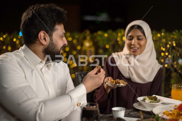 زوجان سعوديان خليجيان على مائدة الافطار بشهررمضان ، مشاركة الاجواء الرمضانية الرائعة بالهواء الطلق ، سفرة مليئة بأصناف من المأكولات العربية السعودية اللذيذة ، شهر رمضان ، رمضان كريم ، فانوس رمضان