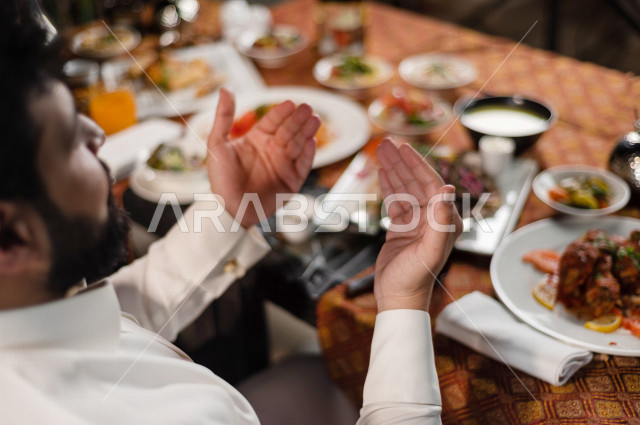 زوجان سعوديان خليجيان على مائدة الافطار بشهررمضان ، رفع اليدين و الدعاء لله بالحمد و الشكر، سفرة مليئة بأصناف من المأكولات العربية السعودية اللذيذة ، شهر رمضان ، رمضان كريم ، فانوس رمضان
