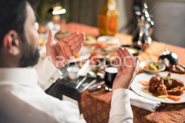 A Saudi Arabian couple at the breakfast table in the month of Ramadan, raising hands and praying to God with praise and thanksgiving, a trip full of varieties of delicious Saudi Arabian food, the month of Ramadan, Ramadan Kareem, Ramadan Lantern