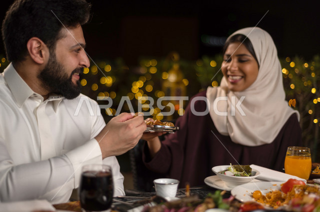 زوجان سعوديان خليجيان على مائدة الافطار بشهررمضان ، مشاركة الاجواء الرمضانية الرائعة بالهواء الطلق ، سفرة مليئة بأصناف من المأكولات العربية السعودية اللذيذة ، شهر رمضان ، رمضان كريم ، فانوس رمضان