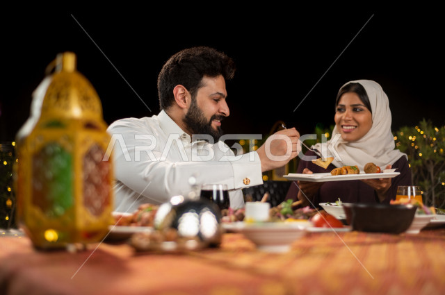 زوجان سعوديان خليجيان على مائدة الافطار بشهررمضان ، مشاركة الاجواء الرمضانية الرائعة بالهواء الطلق ، سفرة مليئة بأصناف من المأكولات العربية السعودية اللذيذة ، شهر رمضان ، رمضان كريم ، فانوس رمضان