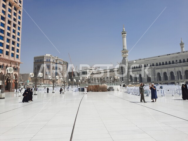 الفن الهندسي المعماري على الطراز الإسلامي للأبراج المحيطة بالحرم المكي الشريف، أداء مناسك الحج والعمرة، الحجاج والمعتمرين في الساحة الخارجية للمسجد الحرام في مكة المكرمة في النهار، معالم دينية إسلامية في المملكة العربية السعودية