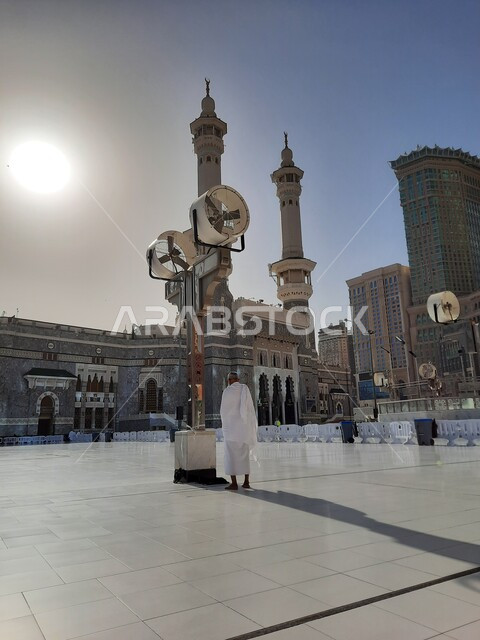 الفن الهندسي المعماري على الطراز الإسلامي للأبراج المحيطة بالحرم المكي الشريف، أداء مناسك الحج والعمرة، الحجاج والمعتمرين في الساحة الخارجية للمسجد الحرام في مكة المكرمة في النهار، معالم دينية إسلامية في المملكة العربية السعودية