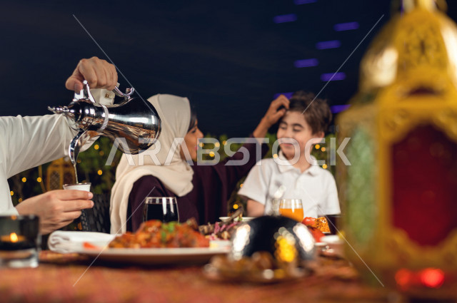 عائلة سعودية خليجية سعيدة على مائدة الافطار بشهررمضان ، شرب القهوة العربية بعد الافطار ، سفرة مليئة بأصناف من المأكولات العربية السعودية اللذيذة ، شهر رمضان ، رمضان كريم ، فانوس رمضان