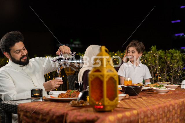 عائلة سعودية خليجية سعيدة على مائدة الافطار بشهررمضان ، شرب القهوة العربية بعد الافطار ، سفرة مليئة بأصناف من المأكولات العربية السعودية اللذيذة ، شهر رمضان ، رمضان كريم ، فانوس رمضان