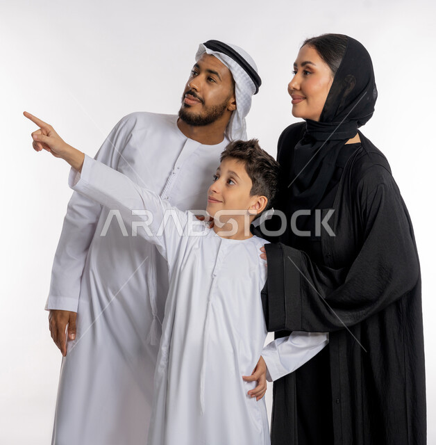 قضاء الأوقات الممتعة برفقة الأسرة, بورتريه أب وأم عربيان خليجيان إماراتيان مع ولدهما الصغير, الاشارة إلى شيء ما بعيد والنظر إليه بإيماءات الاعجاب, لمة العائلة الإماراتية السعيدة, خلفية بيضاء