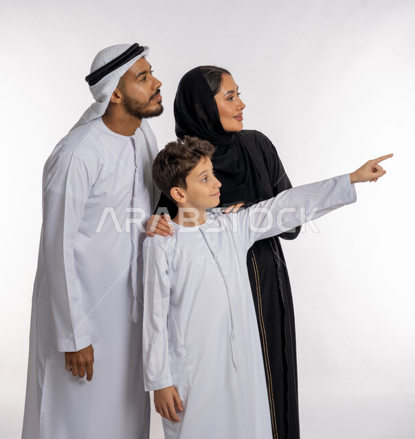 الاشارة إلى شيء ما بعيد والنظر إليه, الترابط الأسري والاستمتاع مع العائلة, قضاء الأوقات برفقة الأبناء, بورتريه أب وأم عربيان خليجيان إماراتيان مع ولدهما بإيماءات الحب والحنان, مفهوم الأسرة الإماراتية السعيدة, خلفية بيضاء